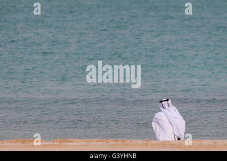 Arabische Mann in traditioneller Kleidung, sitzen am Strand mit Blick auf das Meer Stockfoto