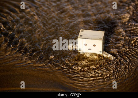 Eine Danbo Danboard Roboter Kunstfigur waten durch tiefes Wasser am Strand Stockfoto