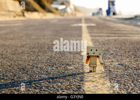 Ein Danbo Danboard Roboter Romanfigur zu Fuß entlang der gelben Linie entlang der Mitte einer Straße Stockfoto