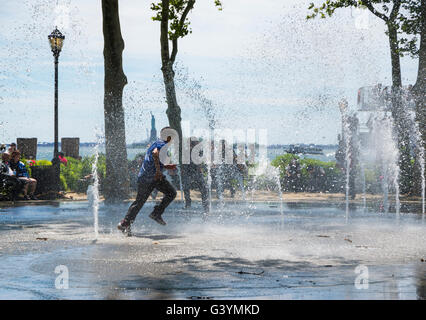 Jungs im Teenageralter läuft durch einen öffentlichen Brunnen und Flickschusterei in Battery Park, New York im Sommer kühl zu halten. Stockfoto