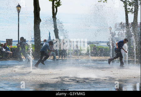 Jungs im Teenageralter läuft durch einen öffentlichen Brunnen und Flickschusterei in Battery Park, New York im Sommer kühl zu halten. Stockfoto