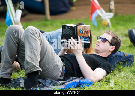 Ein Mann liegt auf dem Rücken ein Buch Besuch Besucher amüsieren sich in die warmen Sonnenstrahlen am Hay Festival der Literatur und Kunst, Heu auf Wye, Powys, Wales UK, Mai 2016 Stockfoto