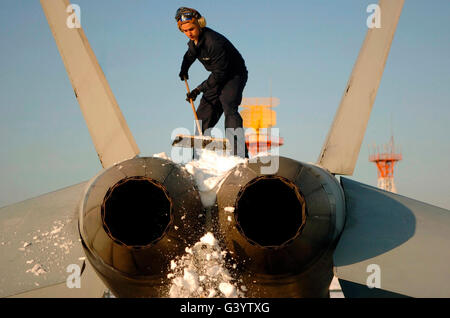 Airman kratzt Schnee von Ende einer F/A-18F Super Hornet. Stockfoto