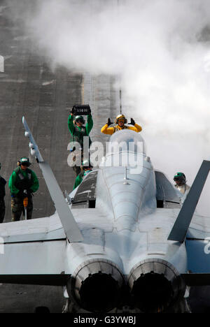 Ein Flugzeug-Handler reiht sich eine F/A - 18C Hornet vor dem abheben. Stockfoto