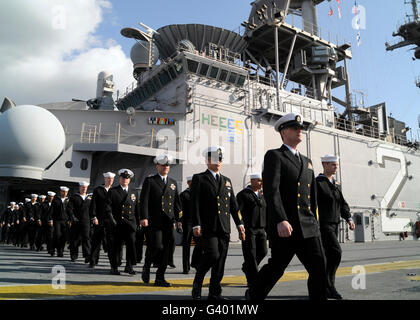 Die Crew der USS Essex marschiert um das Flugdeck um die Schienen zu bemannen. Stockfoto