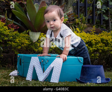 Einjährigen Baby junge Stand in einem Koffer im Garten Stockfoto