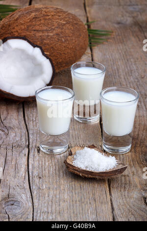 Kokosmilch in einem Glas mit Kokosnuss-Schalen auf alten hölzernen Hintergrund, selektiven Fokus Stockfoto