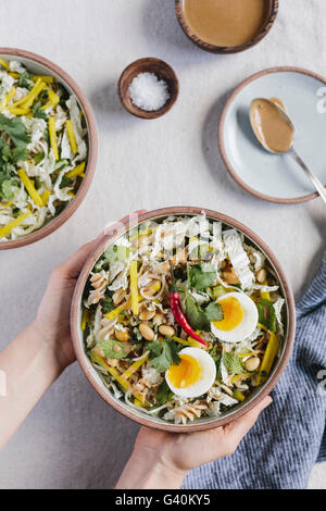 Eine Frau ist eine Schüssel mit knackigen Veggie Schüssel mit warmen Erdnuss Dressing auf dem Tisch platzieren. Stockfoto