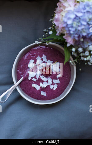 Kirsche Kokos Smoothie in eine graue Schale, garniert mit Kokosflocken und eine ganze Kirsche Stockfoto