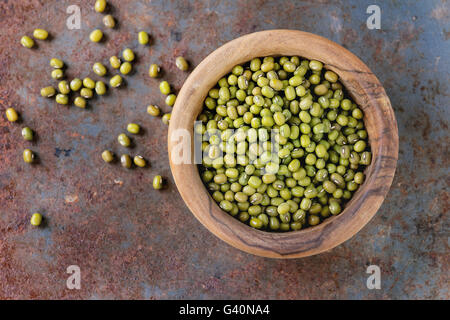 Gesunde Superfood. Ungekocht grünen Mungo Bohnen aus Olivenholz Schüssel über altes rostiges Eisen Hintergrund. Ansicht von oben. Nahaufnahme mit Kopie sp Stockfoto