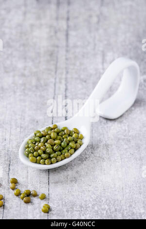 Gesunde Superfood. Ungekocht grünen Mungo Bohnen in weißer Keramik Löffel über weißen hölzernen Hintergrund. Stockfoto