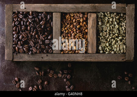 Grüne und braune koffeinfreien ungeröstet und schwarz gerösteten Kaffeebohnen in alten Holzkiste über dunkel braun strukturierten Hintergrund. Ansicht von oben Stockfoto