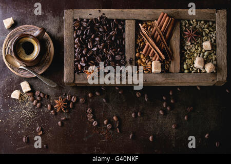 Grüne und braune koffeinfreien ungeröstet und schwarz gerösteten Kaffeebohnen mit Gewürzen und Zucker im alten Holzkiste und Keramik Tasse frisch Stockfoto