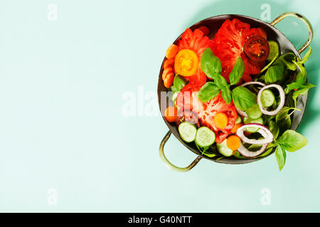 Frischer Salat auf blauem Hintergrund - Tomaten, Zwiebeln, Karotten, Basilikum, Gurken, Salz und Pfeffer. Ansicht von oben Stockfoto