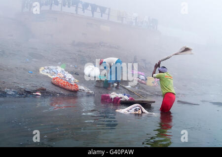 Unbekannter indischer Mann wäscht Kleidung im heiligen Wasser des Flusses Ganges im kalten Nebel alle Stockfoto