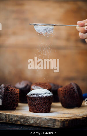 Hand zu sichten Puderzucker auf Schokoladen-Muffins mit einem Tee-Sieb. Stockfoto