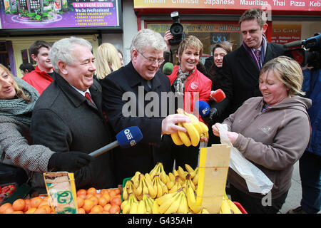 Der irische Labour-Vorsitzende Eamon Gilmore (Mitte) mit dem Kandidaten Joe Costello (links) kauft einen Haufen Bananen von einem Händler in der Moore Street in Dublin, während er im Stadtzentrum von Dublin kampiert. Stockfoto