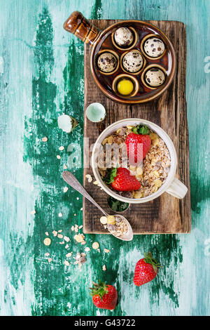 Zutaten für gesundes Frühstück. Wachteleier, Schüssel Müsli und Erdbeeren auf Holz hacken Board Teelöffel über weiß und gr Stockfoto