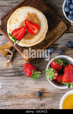 Pfannkuchen mit Erdbeeren und Heidelbeeren, Schalen mit Honig und frischen Beeren über alten hölzernen Hintergrund. Frühstück Konzept backg Stockfoto