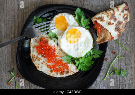 Rührei und Pfannkuchen mit Kaviar auf einer schwarzen Platte Stockfoto