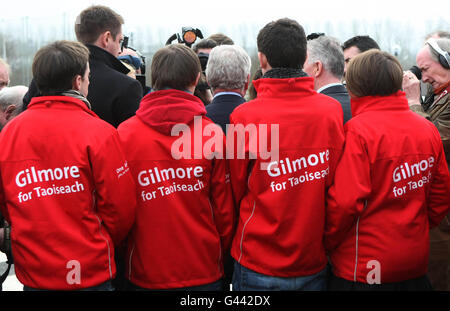 Unterstützer beobachten, wie der irische Labour-Führer Eamon Gilmore vor der Carrick-on-Shannon Community School in Leitrim mit den Medien spricht. Stockfoto