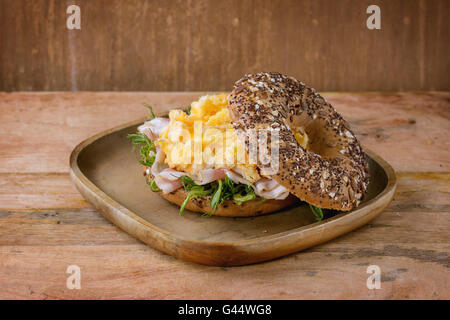 Geöffneten Vollkorn Brötchen mit Rührei, Erbse sprießen und Prosciutto-Schinken auf Holzplatte über hölzerne strukturierten Hintergrund. Stockfoto