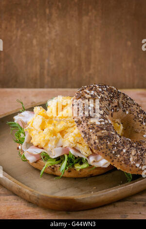 Geöffneten Vollkorn Brötchen mit Rührei, Erbse sprießen und Prosciutto-Schinken auf Holzplatte über hölzerne strukturierten Hintergrund. Stockfoto