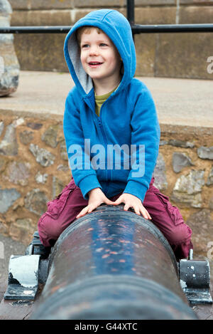 Kleiner Junge sitzt auf einer alten Canon am Hafen in Minehead, Somerset, Großbritannien Stockfoto