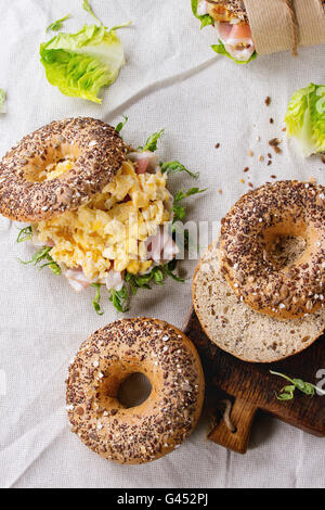 Leeren und Vollkorn-Bagels mit Rührei, Erbse sprießen, gebratenen Zwiebeln und Schinken, auf weißem Leinen Tabelle Personal Stockfoto