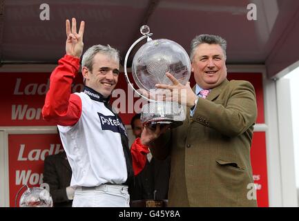 Ruby Walsh (links) feiert mit dem Pokal und Pferdetrainer Paul Nicholls (rechts) nach dem Gewinn der Ladbrokes World Hurdle beim Big Buck's am St. Patrick's Day während des Cheltenham Festivals. Stockfoto