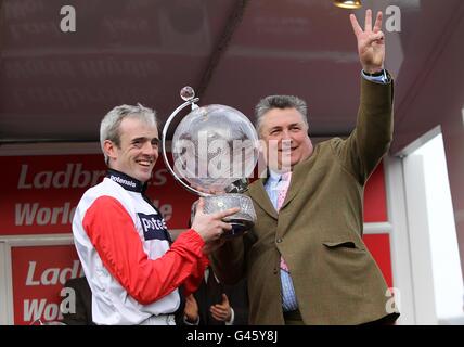 Ruby Walsh (links) feiert mit dem Pokal und Hosre Trainer Paul Nicholls (rechts) nach dem Gewinn der Ladbrokes World Hurdle beim Big Buck's am St. Patrick's Day während des Cheltenham Festivals. Stockfoto