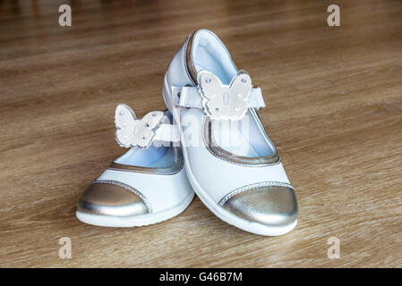 Weiße Schuhe für kleine Mädchen mit Schmetterling-förmige Ornamente auf Holzboden Stockfoto