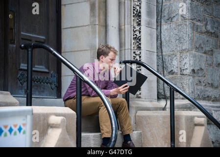 Ein junger Mann sitzt auf der Treppe und Lesebuch, Philadelphia, Pennsylvania, USA Stockfoto