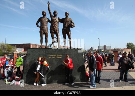 Fans posieren für Fotos mit der United Trinity Statue der ehemaligen Spieler (von links nach rechts) George Best, Denis Law und Bobby Charlton vor Old Trafford Stockfoto