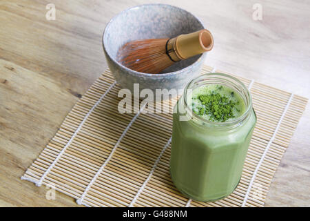 Matcha-Grüntee-Smoothie in Glas mit Stein Schüssel und hölzernen Schneebesen auf Bambusmatte auf obigen Winkel Ansicht Tabelle Stockfoto