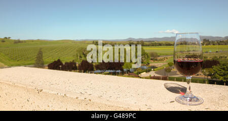 Glas Rotwein auf dem Balkon mit Blick auf Nap Valley Wine Country in Kalifornien. Grünen Bäumen, kleinen Teich und Weinbergen in Mitte Boden Stockfoto