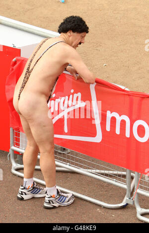 Ein Läufer mit einem „Mankini“ erholt sich nach dem 31. Virgin London Marathon in London. Stockfoto