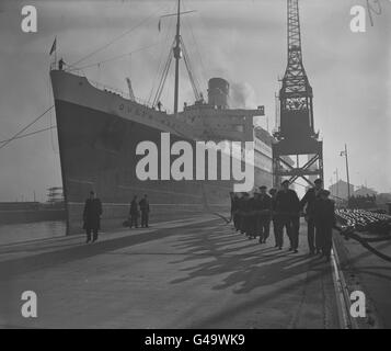 Der 81,000 Tonnen schwere Cunard-White Star-Liner RMS Queen Mary zieht in herrschaftlicher Weise in das King George V Trockendock in Southampton für ihre jährliche Überholung, unterstützt von einer langen Reihe von Hafenarbeitern am Seil. Stockfoto