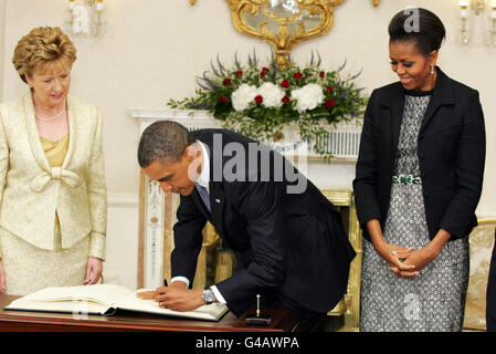 US-Präsident Barack Obama unterschreibt das Besucherbuch, das die irische Präsidentin Mary McAleese (links) und seine Frau, First Lady Michelle Obama, bei seinem Besuch in Irland in Aras an Uachtarain beobachtet haben. Stockfoto