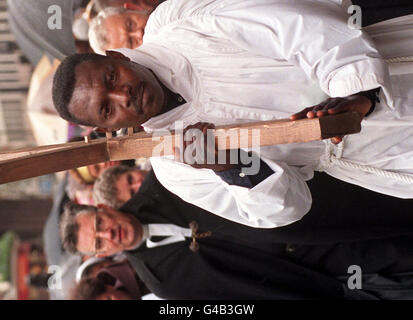 Die sehr Rev Dr. Wesley Carr (links) sieht auf, wie Raphael Mpanzu, ein Flüchtling aus Zaire, trägt das Kreuz bei der jährlichen Kreuzigungsprozession zwischen Methodist Central Hall, Westminster Abbey und Westminster Cathedral in London heute (Freitag). Foto von Ben Curtis/PA. Stockfoto