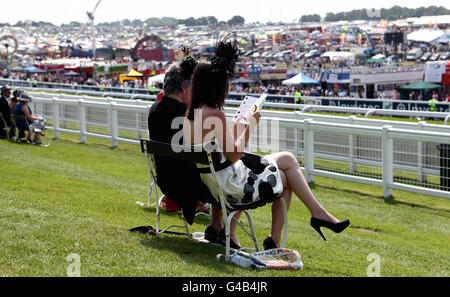 Die Rennfahrer überprüfen die Rennkarte auf dem Rasen im Queens Stand während des Investec Derby Festivals auf der Rennbahn Epsom Downs. Stockfoto