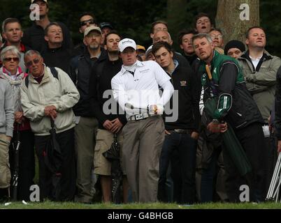 Rory McIlroy und die Menge behalten seinen Ball im Auge, während er beim ersten Lauf der BMW PGA Championship im Wentworth Golf Club, Surrey, aus dem Rough spielt. Stockfoto