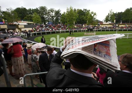 Pferderennen - The Royal Ascot Meeting 2011 - Tag Zwei - Ascot Racecourse. Am zweiten Tag des Royal Ascot Meeting 2011 verbirgt sich unter einer Zeitung neben dem Paradering ein Rennfahrer vor den Elementen. Stockfoto