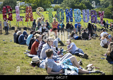 Nachtschwärmer entspannen sich vor dem riesigen „Glastonbury“-Schild im Lounge- und Aussichtbereich des „The Park“ beim Glastonbury-Musikfestival. Stockfoto