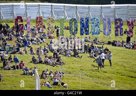 Nachtschwärmer entspannen sich vor dem riesigen „Glastonbury“-Schild im Lounge- und Aussichtbereich des „The Park“ beim Glastonbury-Musikfestival. Stockfoto