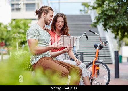-MODELL VERÖFFENTLICHT. Junges Paar sitzt auf Wand mit digital-Tablette. Stockfoto