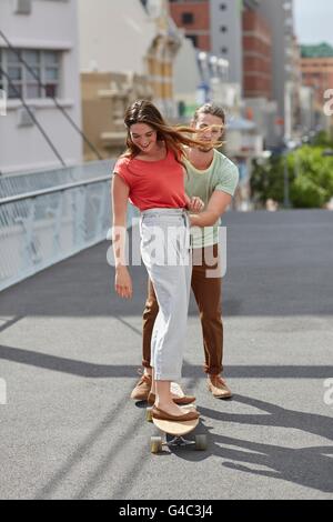 -MODELL VERÖFFENTLICHT. Junge Frau mit Mann schob skateboarding. Stockfoto