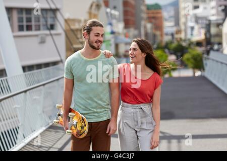 -MODELL VERÖFFENTLICHT. Junges Paar gehen, Mann mit skateboard. Stockfoto