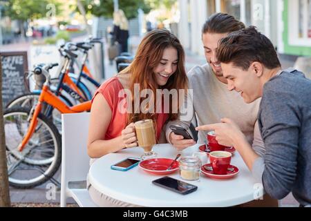 -MODELL VERÖFFENTLICHT. Drei jungen Freunden im Café mit Smartphone. Stockfoto