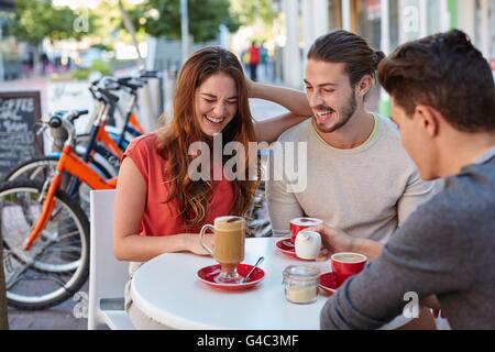 -MODELL VERÖFFENTLICHT. Drei jungen Freunden im Café mit heißen Getränken, lächelnd. Stockfoto